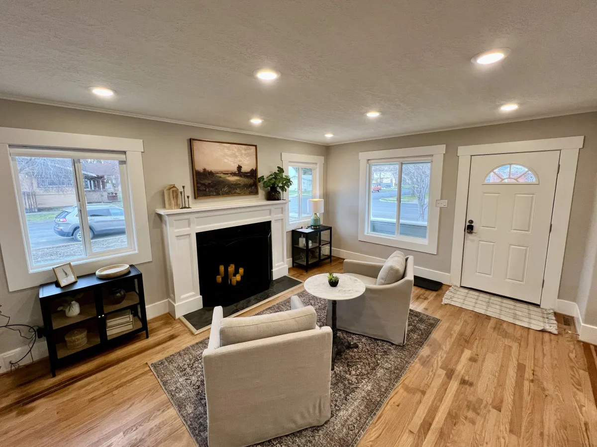 A warm living area with a fireplace, large windows letting in sunlight, and a seating area arranged for socializing or relaxing. The entrance door is also visible, suggesting easy access for pet outings.