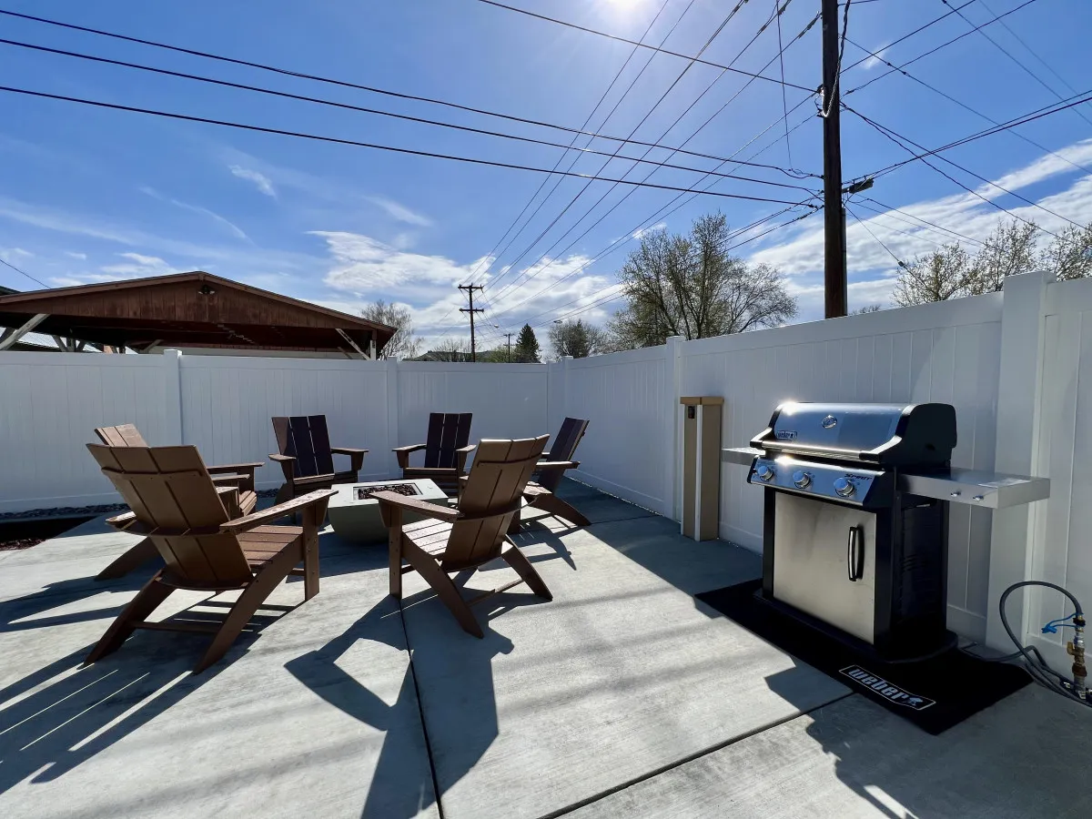 An inviting outdoor dining area featuring a grill, fire pit, and adirondack chairs, all set up for relaxation and social gatherings. The area hints at warmer weather activities, perfect for après-ski evenings or summer barbecues after a round of golf.