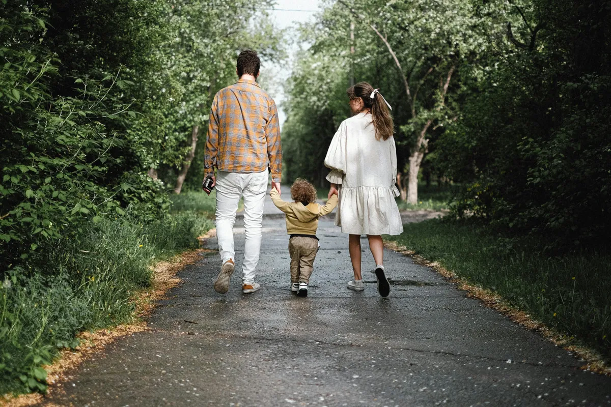 A family, including children, is shown walking together along a tree-lined pathway surrounded by greenery. The mood is cheerful and communal, highlighting outdoor experiences and the ease of exploring local parks and paths.
