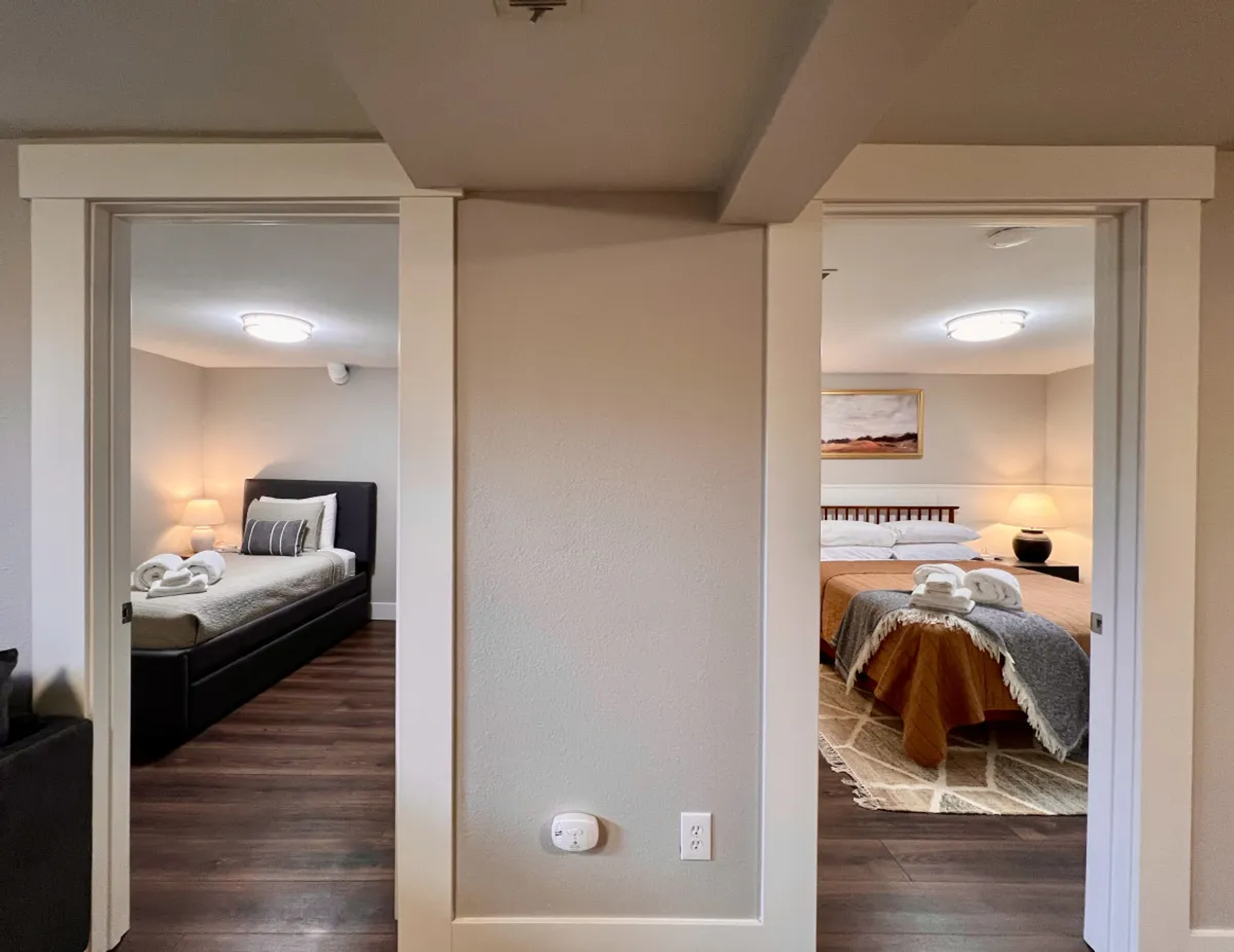 This image presents two adjoining bedrooms, each furnished with comfortable beds, decorative artwork, and soft lighting from bedside lamps. The arrangement highlights both privacy and proximity, suggesting the adaptability of sleeping arrangements for groups or families.