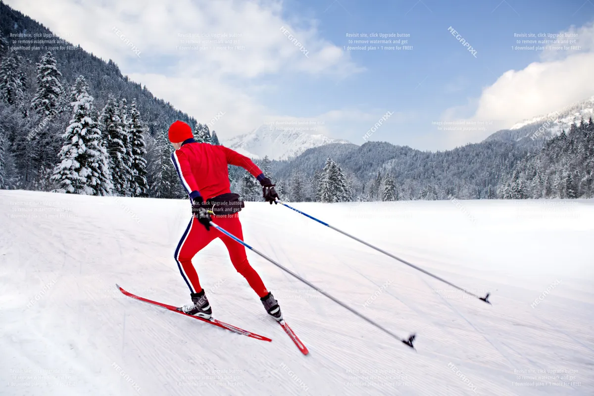 A skier in a bright red outfit glides across a snow-covered landscape, with distant mountains and pine trees creating a scenic winter backdrop. The image exudes a sense of adventure, energy, and the excitement of outdoor winter sports like skiing and cross-country skiing.