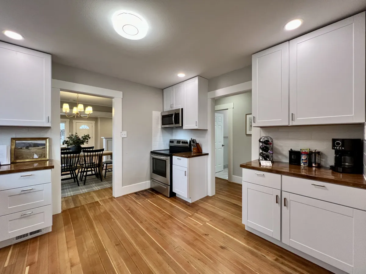 A bright, fully renovated kitchen with contemporary stainless steel appliances, warm wooden countertops, and kitchen cabinets. In the background, a cozy dining area connects seamlessly with the kitchen, reinforcing the open flow of the main floor.