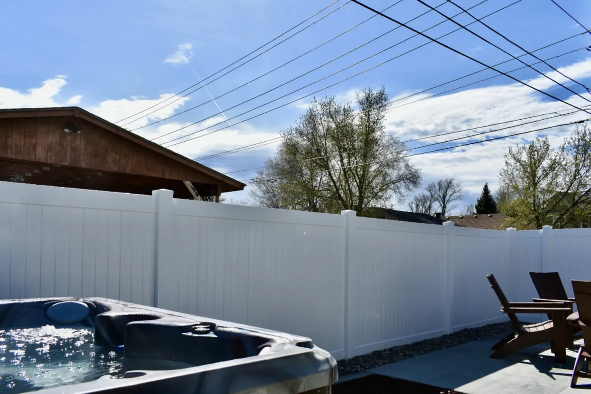 This image shows a tranquil outdoor deck area featuring a hot tub, surrounded by a white fence and wooden decking. The setting is inviting, perfect for both daytime relaxation and evening gatherings, with ample space for socializing or unwinding in privacy.