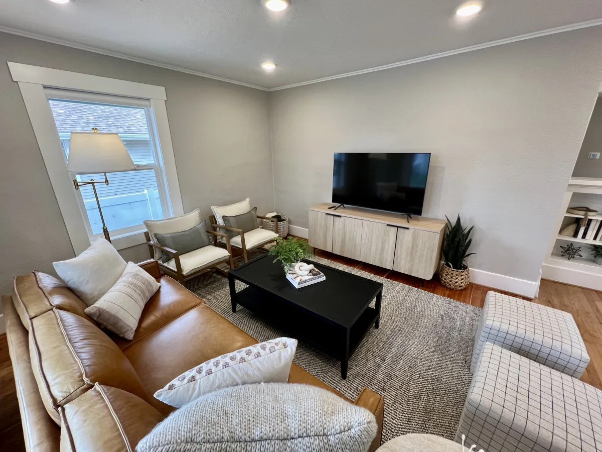 A modern basement living area featuring a leather sofa, coffee table, television, accent chairs, and a decorative plant. The setup appears inviting and comfortable, ideal for group activities like movie nights, relaxing, or socializing.