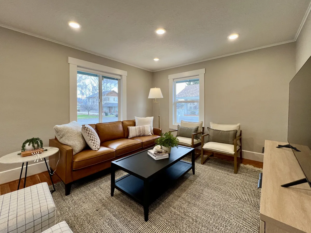 A spacious living area with a leather sofa, coffee table adorned with plants, ample natural light streaming through the window, a floor lamp, and a textured area rug. The room exudes comfort and welcomes both people and pets to relax and socialize.